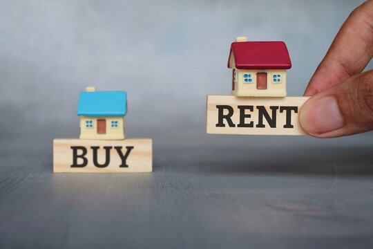Property, real estate, buy and rent concept. Selective focus image of hand pick wooden cube and miniature house with text RENT over wooden cube with text BUY