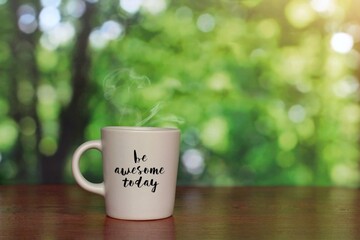 Cup of hot drink with text BE AWESOME TODAY on green bokeh background