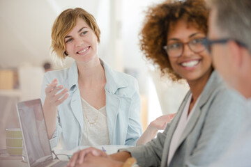 Three office workers talking at desk with laptop