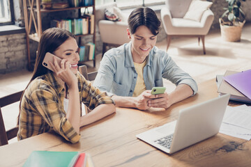 Portrait of two handsome beautiful cheerful learners using device chatting calling at library loft industrial interior indoors