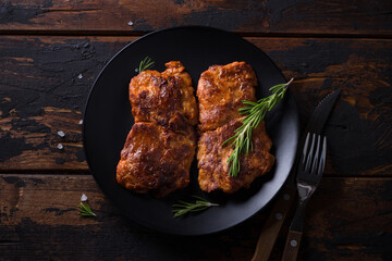 Fried vegan soy steak with rosemary, salt and pepper on black plate on wooden background, top view