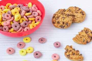 breakfast with bowl of colored cereals with cookies and cocoa powder in the background