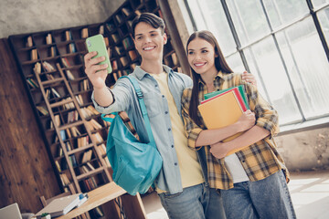 Obraz premium Portrait of two attractive cheerful friends friendship learners hugging taking selfie back to school at loft industrial interior indoors
