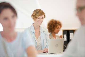 Portrait woman sitting at desk, using laptop smiling in office, colleagues