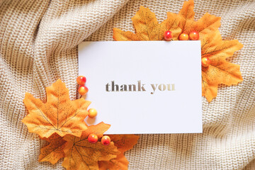 Thank you card on beige knit with yellow maple leaves and autumn berries. Fall theme composition in...