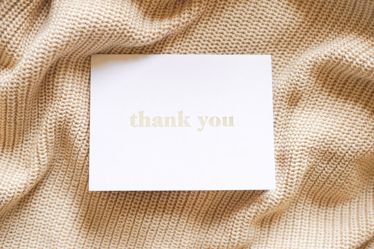 Thank you card on beige knit in natural light. Elegant minimalist composition. Special thank you note.
