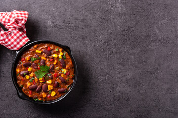 Traditional mexican tex mex chili con carne in iron pan on black background. Top view. Copy space