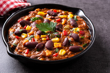 Traditional mexican tex mex chili con carne in iron pan on black background