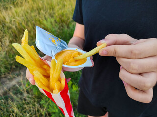 Girl eating french fries, dipping in sauce outdoor