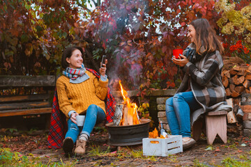 three friends relax comfortably and drink wine on an autumn evening in the open air by the fire in...