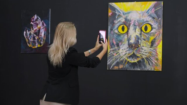 woman is taking photo by smartphone of modern abstract picture in fine art museum