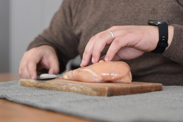 man with watch cutting a chicken breast on a board at the kitchen table