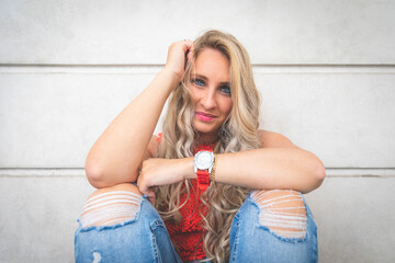 Une blonde sourit assise contre un mur de béton