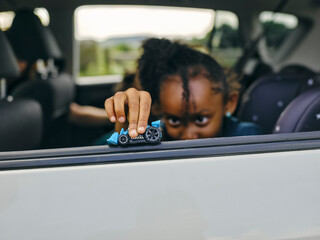 Girl sitting in back seat and playing with toy car