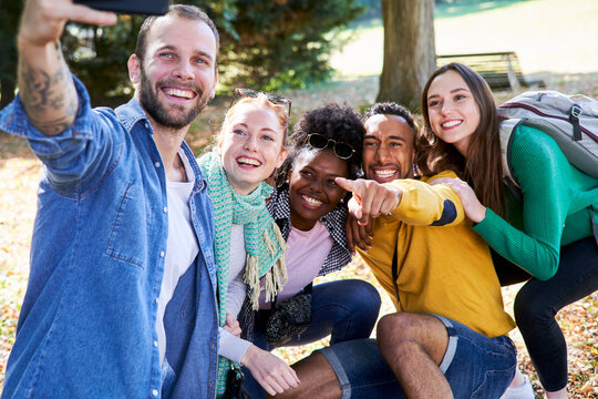Smiling man taking selfie with smart phone while standing with friends in park