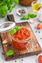 Traditional Italian marinara sauce in a jar on a concrete background with spices and ingredients. Copy space.