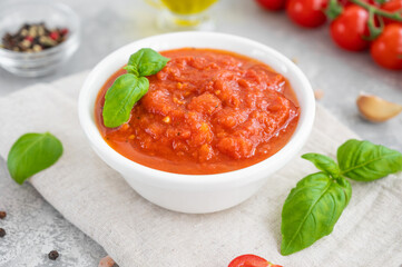 Traditional Italian marinara sauce in a bowl on a concrete background with spices and ingredients. Copy space.