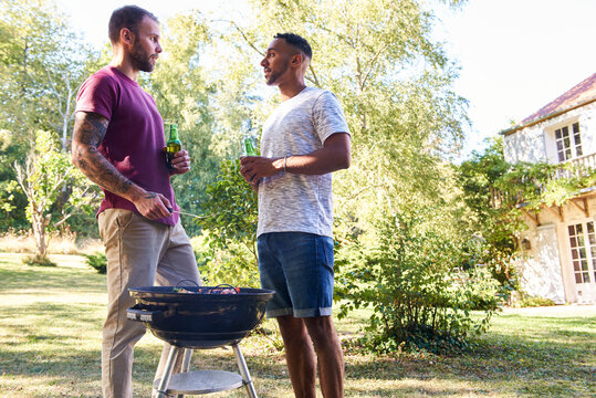 Young men with beer bottles standing near barbecue grill