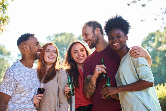 Smiling young friends standing with beer bottles and wine glass in garden
