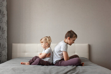 brother and sister have quarreled and sitting with their backs to each other home on bed. concept childhood, family