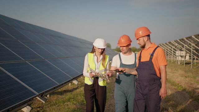 Diverse engineers man and woman inspecting solar panels on photovoltaic power plant outdoors. Couple of workers cooperating controlling clear power energy production. Solar panels field. Ecological