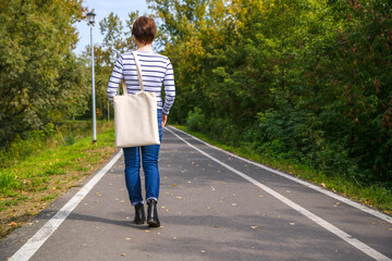 Fototapeta premium Woman holding tote bag walking in the park mockup