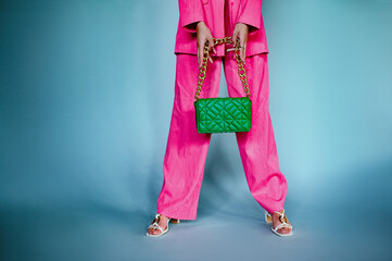 Trendy summer fashion details: woman wearing wide leg pink fuchsia trousers, strappy sandals, holding green leather quilted cassette bag, handbag with chunky chain. Copy, empty space for text