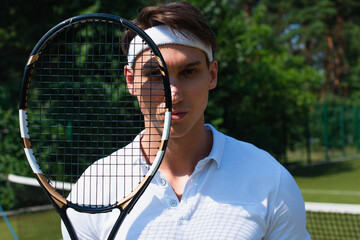 Young sportsman holding tennis racket and looking at camera