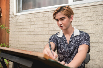 A young asian draftsman or architecture student siting on a drafting table, using a t-square to...