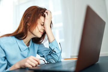 tired woman sitting at a table in front of a laptop work dissatisfaction