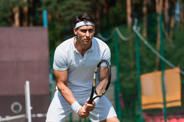 Concentrated sportsman holding tennis racket on court outdoors