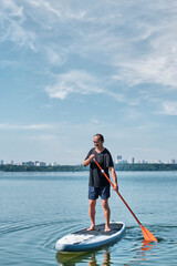 Asian older man on sup board on calm lake.