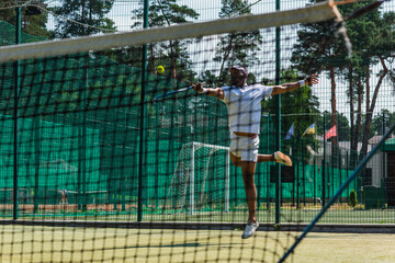 African american sportsman jumping while playing tennis near net