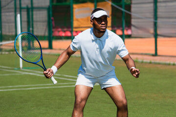 Focused african american sportsman playing tennis on court