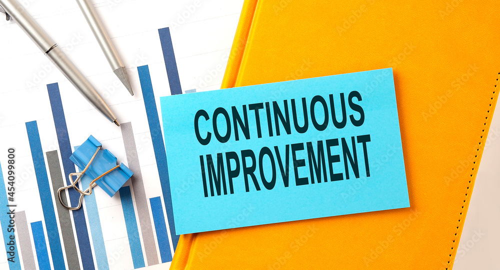 Poster continuous improvement text on sticker on the yellow notebook with chart and pen