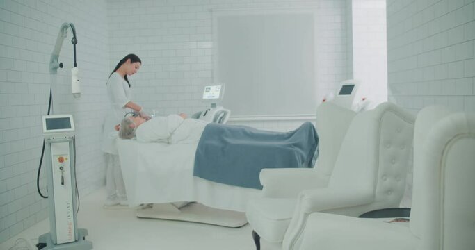 A close-up female cosmetologist is doing a SMAS lifting procedure on the female client by using the Ultraformer apparatus.