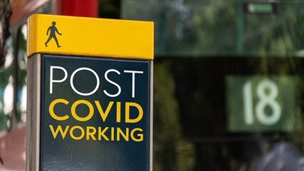 Post Covid working sign in a busy commuter city center