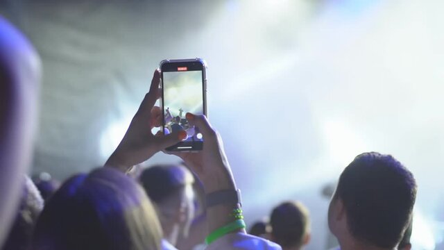 Hand with a smartphone records music festival and taking photo of concert stage.