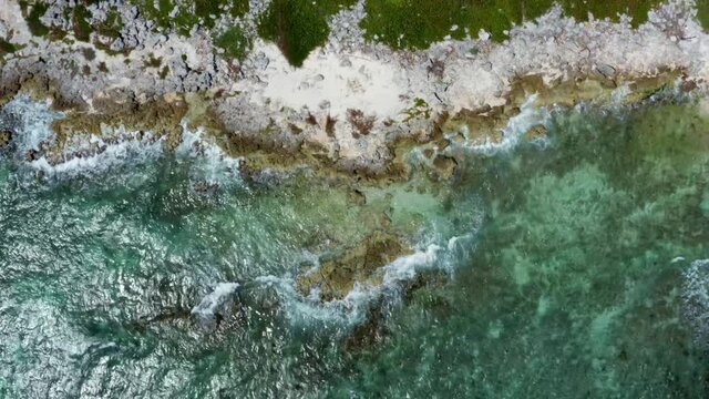 Beautiful right truck aerial bird's eye drone view of a tropical barren beach with clear turquoise water, white sand, palm trees, and waves crashing into rocks near Riviera Maya, Mexico near Cancun.