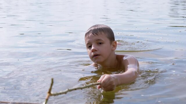 Active Child Playing with a Stick in River, in Water Creating Waves, Splashes. Happy boy enjoys playing with water drops. Teenager bathes in a pond in summer. Water procedures, rest on nature. 4K.