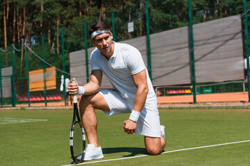 Focused sportsman holding racket while kneeling on court