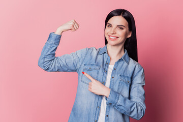 Close-up portrait of pretty cute cheerful girl point finger strong arm muscle isolated on pink...