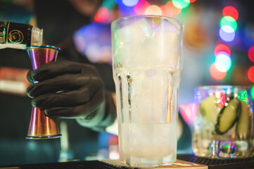 hands of a bartender with black gloves making cocktail on a bar counter.