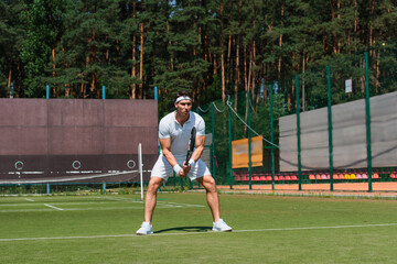 Sportsman in white sportswear holding tennis racket on court