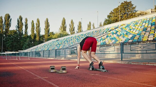 Rear view, young male athlete starts hurdle race. Sprint run, stop block