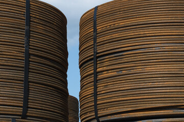 Several bunches of rolled rusty structural steel against a blue sky