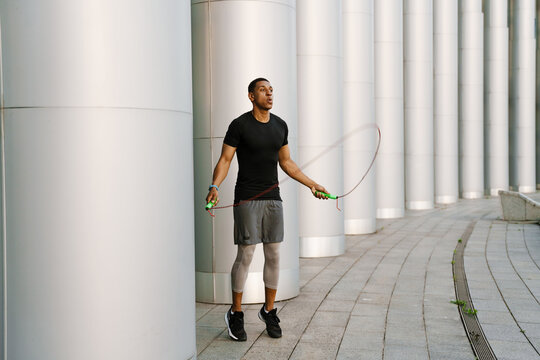 Black sportsman working out with jumping rope outdoors