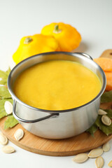 Pot with pumpkin soup and ingredients on white background