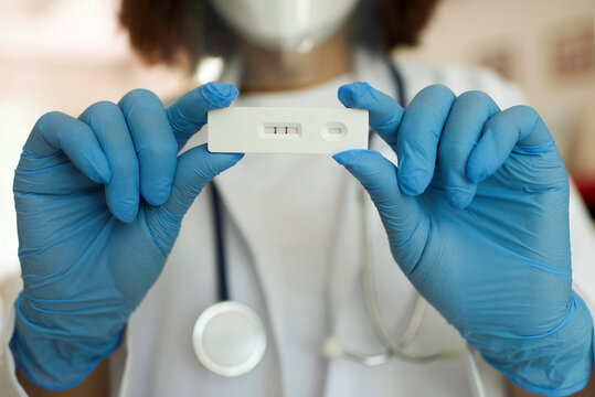 Asian doctor wearing blue gloves and hygiene protective face mask holding SARS 2019-nCoV COVID-19 coronavirus antigen rapid test kit - ag test with positive result. Home kit. Close up.Laboratory.