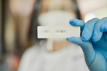 Asian doctor wearing blue gloves and hygiene protective face mask holding SARS 2019-nCoV COVID-19 coronavirus antigen rapid test kit - ag test with negative result. Home kit. Close up.Laboratory.